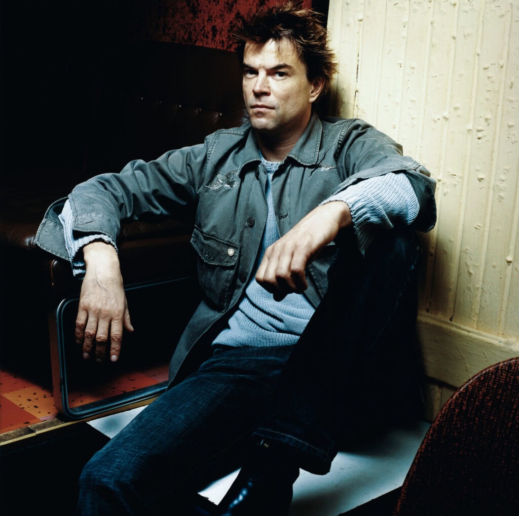 Frank Siemers sitzt entspannt in einem stilvollen Raum, getragen von lebendigen Farben und warmem Licht.