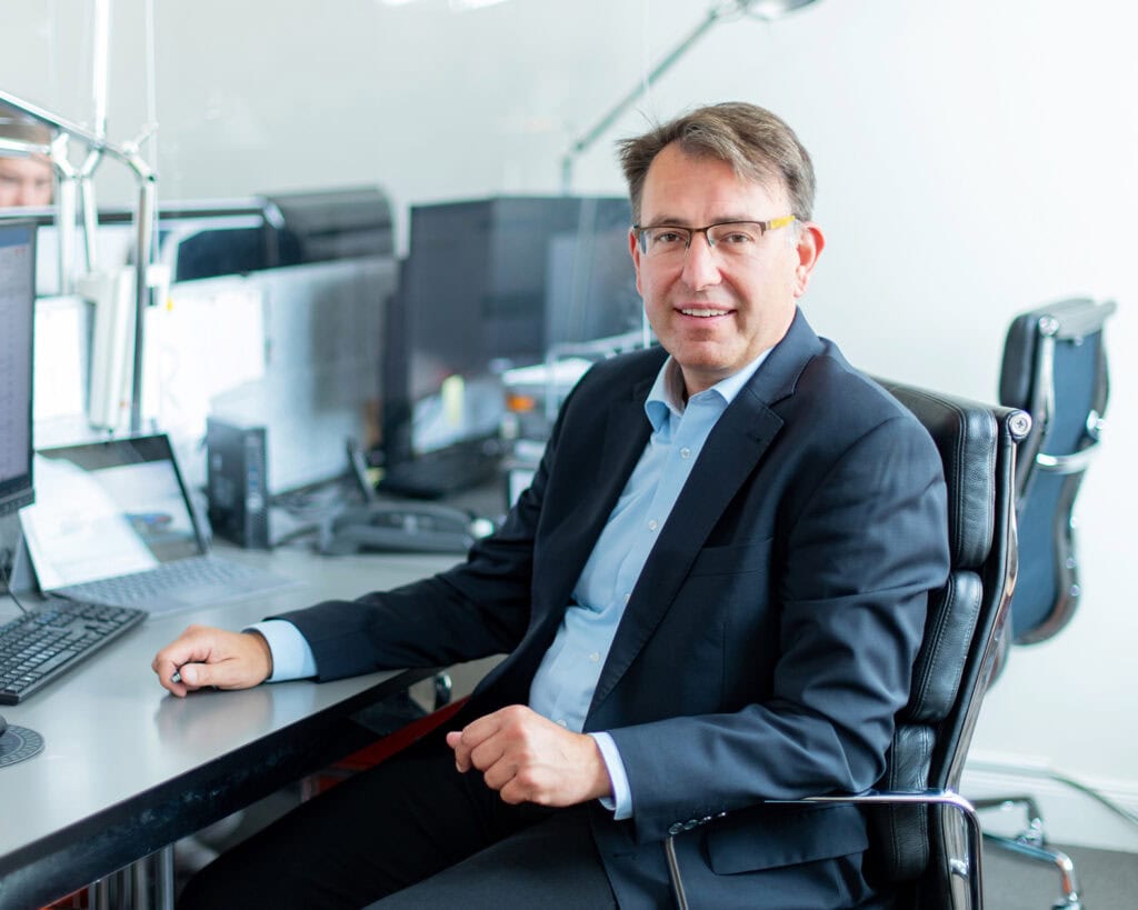 Hochwertiger Businessporträtfotografie eines Mannes in einem modernen Büro, der professionell im Anzug an seinem Arbeitsplatz sitzt.