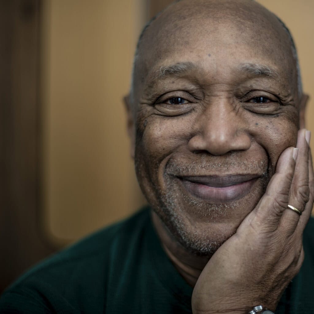 Porträt eines lächelnden älteren Mannes mit dunkler Haut, Nahaufnahme, warmes Licht, Ausdruck von Gelassenheit und Freude, professionell fotografiert von Frank Siemers.
