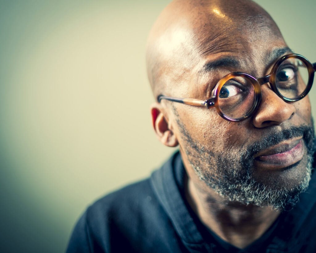 Nahaufnahme eines Mannes mit runden Brillengläsern und grauem Bart, der direkt in die Kamera schaut.