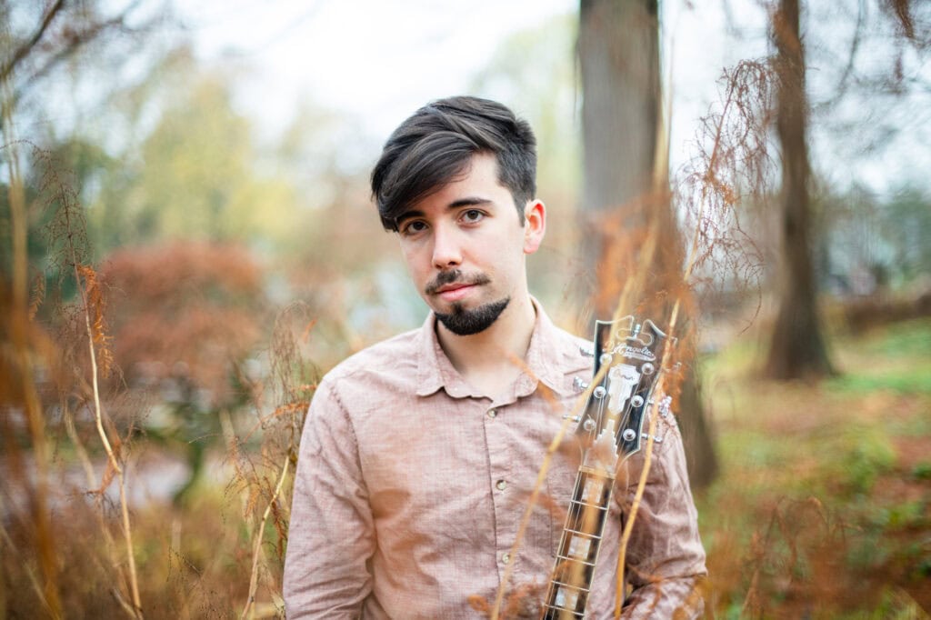 Französischer Musiker mit E-Gitarre in einem herbstlichen Wald.