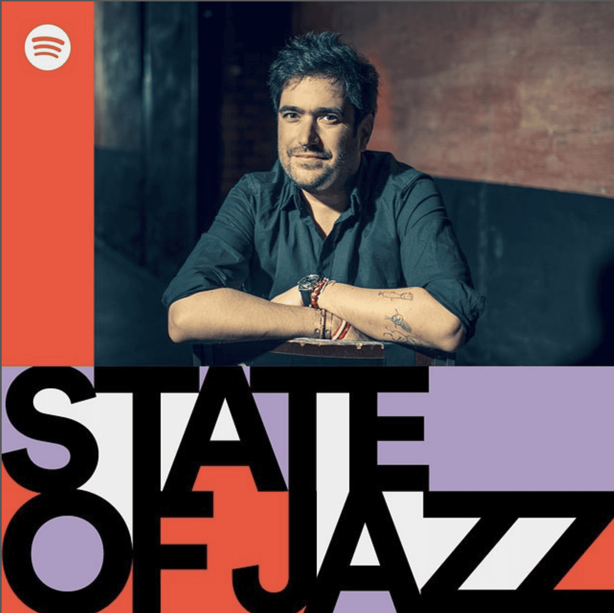 Porträt eines lächelnden Mannes mit dunklem Haar, sitzend in einem stilvollen Lounge-Bub, hinter einem dunklen Graffiti-Hintergrund.