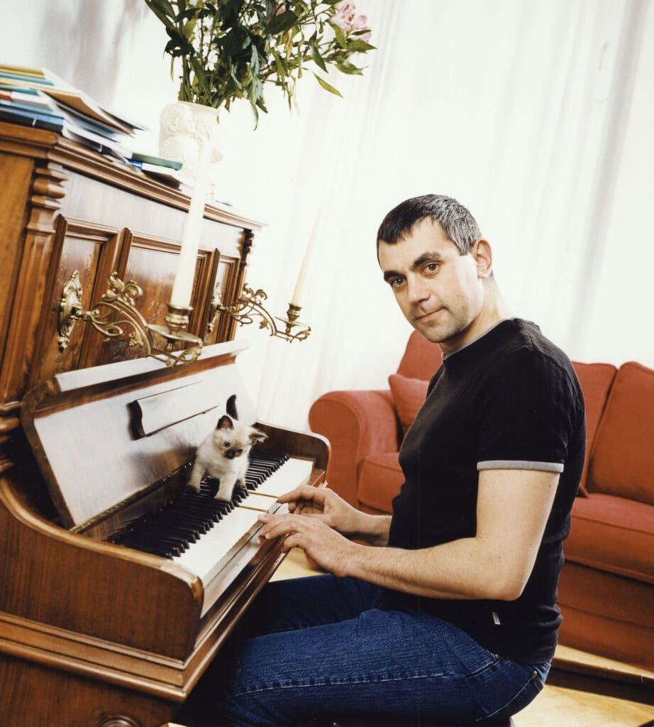 Hauptbild eines Mannes am alten Klavier mit Katze, im Wohnzimmer, natürlicher Lichtschein, detailreiche Porträtaufnahme.