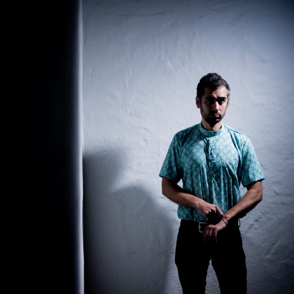 Menschenporträt in einem dunklen, künstlerischen Licht, das den Mann vor einer weißen Wand hervorhebt.