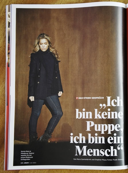 Ich bin keine Puppe, ich bin ein Mensch – Porträt einer selbstbewussten Frau in einem modischen Outfit vor braunem Hintergrund.