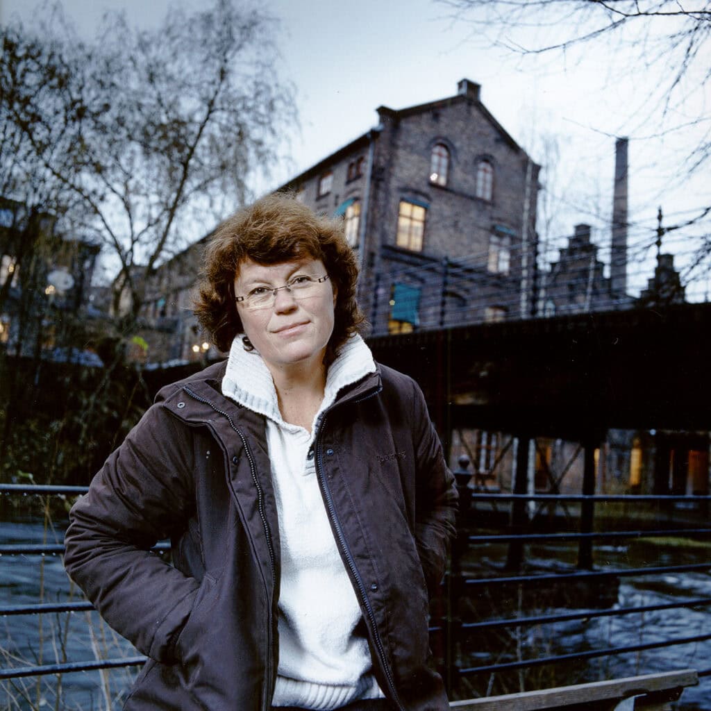 Archivierte Aufnahmaufnahme einer Frau in einer schwarzen Jacke vor einem Wasserlauf in Hamburg, im Hintergrund alte Backsteingebäude bei Dämmerung, professionelle Portraitfotografie von Frank Siemers.